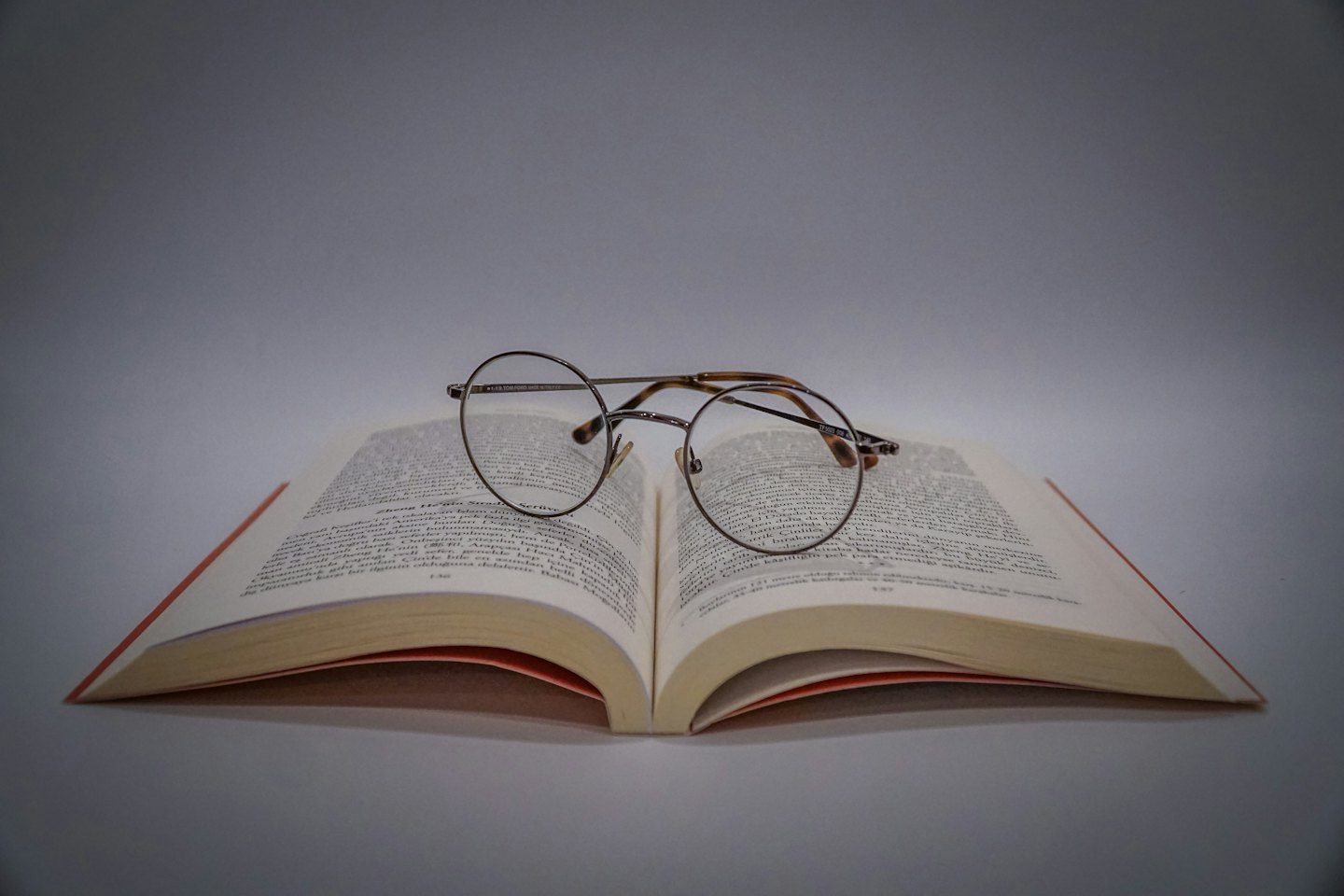 Open book with reading glasses on a grey surface.