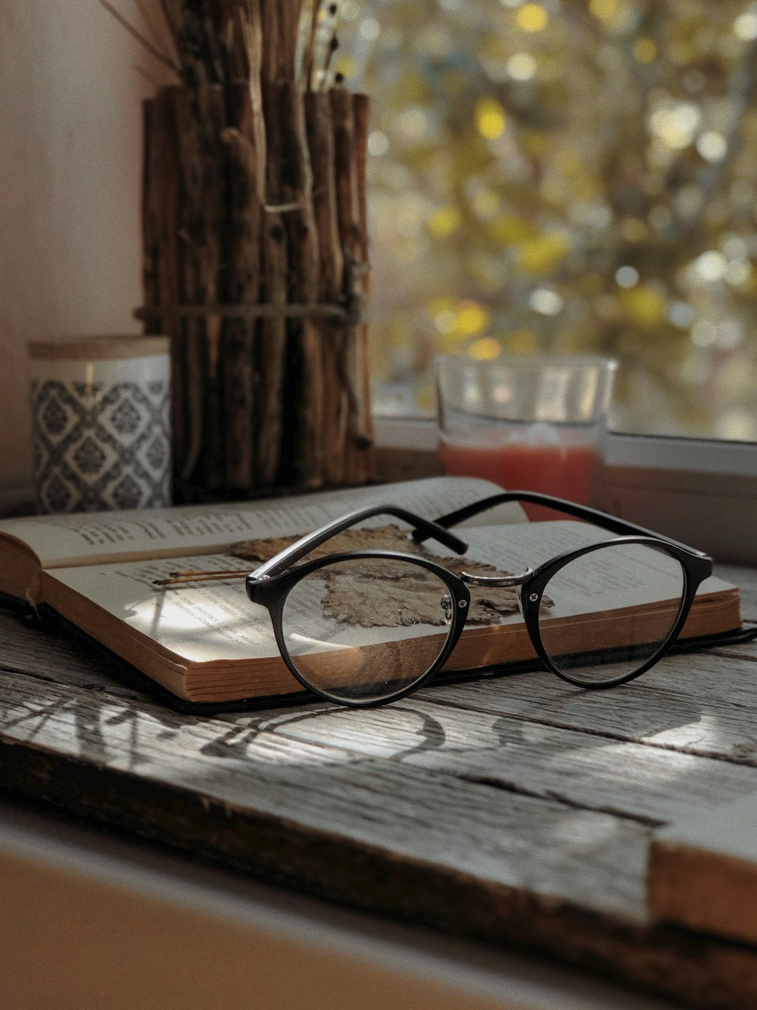 Reading glasses sit on an open book on a wooden table.